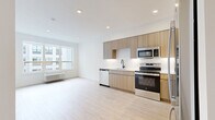 This thoughtfully designed one-bedroom, one-bathroom unit at 74 Freeman Street in Newark, NJ offers a clean, modern aesthetic throughout its efficiently laid-out single floor. Light-toned hardwood flooring runs continuously across the living areas, kitchen, and bedroom, creating a cohesive and bright interior.

The open-concept kitchen is a standout feature, outfitted with flat-front light wood cabinetry extending to the ceiling for ample storage, white quartz countertops, a white tile backsplash with under-cabinet lighting, and a full suite of stainless steel appliances including a French door refrigerator, electric range, built-in microwave, and dishwasher. A matte black faucet at the sink adds a refined contrast to the light palette.

The living area benefits from large windows that invite natural light and offer views of the surrounding urban environment. A wall-mounted PTAC unit provides individual climate control. The bedroom is a comfortable, well-proportioned space with its own window fitted with a roller shade and a dedicated PTAC unit.

A hallway connects the bedroom, a dedicated closet with an in-unit stacked washer and dryer, and the full bathroom. The bathroom features tile flooring, a soaking tub with white subway tile surround, a vanity with a white countertop, a mirrored medicine cabinet, and matte black fixtures throughout.
