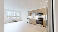 This thoughtfully designed one-bedroom, one-bathroom unit at 74 Freeman Street in Newark, NJ offers a clean, modern aesthetic throughout its efficiently laid-out single floor. Light-toned hardwood flooring runs continuously across the living areas, kitchen, and bedroom, creating a cohesive and bright interior.

The open-concept kitchen is a standout feature, outfitted with flat-front light wood cabinetry extending to the ceiling for ample storage, white quartz countertops, a white tile backsplash with under-cabinet lighting, and a full suite of stainless steel appliances including a French door refrigerator, electric range, built-in microwave, and dishwasher. A matte black faucet at the sink adds a refined contrast to the light palette.

The living area benefits from large windows that invite natural light and offer views of the surrounding urban environment. A wall-mounted PTAC unit provides individual climate control. The bedroom is a comfortable, well-proportioned space with its own window fitted with a roller shade and a dedicated PTAC unit.

A hallway connects the bedroom, a dedicated closet with an in-unit stacked washer and dryer, and the full bathroom. The bathroom features tile flooring, a soaking tub with white subway tile surround, a vanity with a white countertop, a mirrored medicine cabinet, and matte black fixtures throughout.