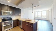 Located at 7911 Westpark Dr in McLean, Virginia, this modern one-bedroom residence offers a well-appointed, single-floor layout designed for comfortable urban living. The entry foyer features rich dark hardwood-style tile flooring and provides immediate access to a full bathroom finished with warm stone tile walls and a soaking tub. The open-concept kitchen is a standout feature, showcasing dark espresso cabinetry extending to the ceiling, granite countertops, a travertine tile backsplash, and a full suite of stainless steel appliances including a double oven range and built-in dishwasher. A central island with a double sink and pendant lighting connects the kitchen seamlessly to the living area. The living room is bright and airy, highlighted by floor-to-ceiling windows that flood the space with natural light and frame expansive views of the McLean and greater Northern Virginia skyline. Light hardwood-style flooring runs throughout the living areas. The bedroom offers plush carpeting, a ceiling fan, a private balcony access door with sweeping outdoor views, and a generously sized walk-in closet outfitted with built-in shelving and hanging rods. The overall ambiance is clean, contemporary, and light-filled throughout.