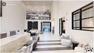 This expansive single-floor amenity space delivers an impressive blend of contemporary design and functional versatility across a generously scaled floor plan. The grand lobby entrance sets the tone immediately, showcasing soaring double-height ceilings, bold black-and-white striped tile flooring, and a striking large-format aerial photography mural mounted high on the wall. A reception desk anchors the space, while seating areas with modern furnishings invite guests to linger.

The living room area features a dramatic accent wall with an intricate dark geometric pattern, white sectional seating, and sculptural black coffee tables, creating a stylish social hub. Nearby, a dedicated office area impresses with floor-to-ceiling vertical light fixtures, marble-clad surfaces, and an executive desk arrangement framed by coffered architectural detailing.

The kitchen and living room combine into a showpiece gathering area, centered on an expansive marble-topped island with bar seating and gold-toned pendant lighting suspended above. Herringbone wood-look flooring, navy cabinetry, and a full appliance suite complete this chef-quality space.

A game room offers foosball, shuffleboard, and card tables beneath soaring ceilings and a statement pendant fixture. Additional lounges provide tufted booth seating for co-working or socializing, while hallways and a laundry room round out the thoughtfully designed layout.