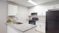 This two-floor residence offers a clean, modern aesthetic with thoughtful finishes carried consistently throughout the space. The kitchen is a standout feature, showcasing crisp white shaker cabinetry, granite-patterned countertops, a stainless steel sink set into a peninsula, and black appliances including a range and refrigerator. Light wood-look flooring grounds the kitchen and connects seamlessly to adjacent areas, while recessed overhead lighting keeps the space bright and functional.

A carpeted staircase with a black metal railing connects the two floors, adding a contemporary touch to the transition between levels. The upper floor hosts multiple generously sized bedrooms, each finished with plush neutral carpet, ceiling fans with integrated lighting, and windows fitted with white horizontal blinds that allow for natural light and privacy. The open corner window configurations in select bedrooms enhance the sense of airiness throughout.

The bathroom continues the home's cohesive design language, featuring granite-topped white vanity cabinetry, a wall-mounted mirror with vanity lighting, light wood-look flooring, and a separate tub-shower enclosure with tile surround. Neutral gray walls and clean white trim unify the interior, creating a calm and move-in-ready environment across both floors.
