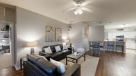 Located at 2614 W Tennessee St in Tallahassee, Florida, this single-floor residence offers a well-designed, open-concept layout with distinct living, dining, and kitchen areas that flow seamlessly together. The living room features vaulted ceilings, rich dark hardwood flooring, and a ceiling fan, creating a comfortable and airy atmosphere. A sliding glass door provides access to an outdoor area and allows natural light to fill the space. The dining area connects directly to the living room, complemented by track lighting and decorative wall art. The kitchen is equipped with white cabinetry, a tile backsplash, stainless steel appliances including a range, microwave, and refrigerator, and a breakfast bar with counter seating — all set atop light tile flooring. The bedrooms offer a cozy retreat, each with large windows that invite natural light. The bathrooms are finished with wood-look flooring, white vanities with ample counter space, large mirrors, and one bathroom features an oversized garden bathtub with tile surround. A second full bathroom includes a dual-sink vanity with crisp white countertops and modern fixtures. Throughout the space, neutral gray walls provide a versatile backdrop, lending a clean and contemporary feel to every room.
