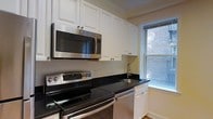 This single-floor space includes a thoughtfully designed kitchen that balances functionality with a clean, classic aesthetic. The kitchen is outfitted with a full suite of stainless steel appliances, including an electric range with a smooth cooktop, an over-the-range microwave, and a dishwasher. Dark granite countertops provide a striking contrast against the crisp white raised-panel cabinetry, which extends to the upper walls to maximize storage. A stainless steel undermount sink is positioned near a window that overlooks an exterior brick façade, allowing natural light to filter into the space. The hardwood flooring adds warmth and continuity throughout. The white painted walls and bright cabinetry contribute to an open, airy feel despite the kitchen's compact footprint. Overall, the kitchen is efficiently laid out, making practical use of available space while maintaining a polished, well-maintained appearance suited for everyday cooking and meal preparation.