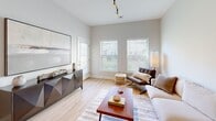 Located at 1100 Jericho Turnpike in Commack, NY, this one-bedroom, one-bathroom unit offers a well-designed single-floor layout with a thoughtful use of space throughout. Light wood-look flooring flows seamlessly across all rooms, creating a cohesive and warm aesthetic complemented by a neutral color palette of soft whites and grays.

The open-concept kitchen and living area serves as the heart of the unit. The kitchen is equipped with white shaker cabinetry extending to the ceiling, a classic subway tile backsplash, stainless steel appliances including a refrigerator, range, and microwave, and a white quartz peninsula with bar seating illuminated by pendant lighting. Track lighting adds a modern functional touch overhead.

The living room benefits from multiple windows that invite natural light and provide outdoor views, contributing to an airy and bright atmosphere. High ceilings further enhance the sense of openness throughout this shared space.

The bedroom is a well-proportioned retreat featuring a large window with exterior views, light wood flooring, and dual doors providing access to a dedicated closet with built-in shelving and hanging rods for ample storage.

The bathroom is cleanly finished with a white shaker vanity, framed mirror, and light wood flooring, maintaining the consistent modern aesthetic found throughout the unit.