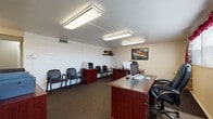 Located at 549 Fifth Street SE Ln in Barberton, Ohio, this single-floor commercial property offers a versatile and well-organized layout suitable for a variety of professional uses. The main office area is equipped with multiple workstations, mahogany-finished desks, and overhead fluorescent lighting that ensures a bright, productive environment. A row of seating along the wall serves as a dedicated waiting area within the office, complemented by a printer station and wall-mounted artwork. A separate lounge-style waiting room features tufted black leather chairs arranged around a glass-top coffee table, providing a comfortable reception space for visitors. A hallway connects the main areas to several private rooms with paneled doors, offering flexibility for individual offices or consultation spaces. The property also includes a functional galley-style kitchen outfitted with a gas range, full-size refrigerator, wood-trimmed countertops, and ample cabinetry with durable tile flooring. A dedicated laundry room houses multiple washing machines and a row of private storage stalls, adding operational convenience. Throughout the space, neutral-toned walls, carpeted floors in office areas, and practical lighting fixtures contribute to a clean, professional ambiance.