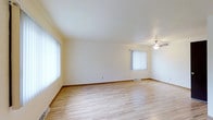 This multi-story property spans three floors, offering a well-organized and functional layout throughout. The interior is characterized by a bright, neutral color palette with crisp white walls and ceilings that enhance the sense of openness in each room. The flooring features light-toned hardwood-style planks that run throughout, adding warmth and continuity to the space. Large windows dressed with vertical blinds allow generous amounts of natural light to filter in, creating an airy and welcoming atmosphere. A ceiling fan provides both practical ventilation and a subtle design accent in the main living area. The open layout of the primary living space offers flexibility for a variety of furniture arrangements. Baseboard trim and floor vents reflect a straightforward, clean architectural style. The three-floor configuration provides distinct zones for living, sleeping, and utility purposes, making efficient use of the available vertical space. Overall, the property presents a tidy, move-in-ready environment with a modest and practical design sensibility suited to a range of occupants.
