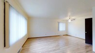 This multi-story property spans three floors, offering a well-organized and functional layout throughout. The interior is characterized by a bright, neutral color palette with crisp white walls and ceilings that enhance the sense of openness in each room. The flooring features light-toned hardwood-style planks that run throughout, adding warmth and continuity to the space. Large windows dressed with vertical blinds allow generous amounts of natural light to filter in, creating an airy and welcoming atmosphere. A ceiling fan provides both practical ventilation and a subtle design accent in the main living area. The open layout of the primary living space offers flexibility for a variety of furniture arrangements. Baseboard trim and floor vents reflect a straightforward, clean architectural style. The three-floor configuration provides distinct zones for living, sleeping, and utility purposes, making efficient use of the available vertical space. Overall, the property presents a tidy, move-in-ready environment with a modest and practical design sensibility suited to a range of occupants.