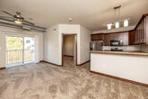 This single-floor unit offers a well-organized layout that balances open communal spaces with defined private areas. The living room is a comfortable, carpeted space highlighted by an exposed metal ductwork detail along the ceiling, adding an industrial touch. A ceiling fan provides additional airflow, while a sliding glass door opens to a private balcony overlooking surrounding greenery, allowing natural light to fill the room.

The kitchen is well-appointed with rich, dark-stained wood cabinetry extending to the ceiling for ample storage, complemented by stainless steel appliances including a refrigerator with ice maker, electric range, and dishwasher. Stone-toned countertops and tile flooring complete the practical yet attractive workspace. A peninsula with pendant lighting provides a casual dining or prep area that connects the kitchen to the living space.

The bedrooms are carpeted and generously sized, each featuring closets with built-in shelving. The full bathroom includes a tub-shower combination, a wood-vanity with light countertop, tile flooring, and brushed nickel fixtures. A dedicated in-unit laundry room with wire shelving and tile flooring adds everyday convenience to this thoughtfully designed space.
