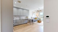 This efficiently designed one-bedroom, one-bathroom residence makes excellent use of its compact footprint across a single floor. The open-concept layout seamlessly connects the kitchen, dining area, and living room, creating a cohesive and functional living space. The kitchen is outfitted with sleek gray shaker-style cabinetry extending to the ceiling, a light stone countertop, stainless steel appliances including a gas range and oven, and a textured tile backsplash. A compact dining table with bar stools serves as a natural transition between the kitchen and living area. The living room is bright and welcoming, anchored by large sliding glass doors that open to a private balcony offering open city views. Light hardwood flooring runs throughout, enhancing the airy feel of the space. The bedroom is a serene retreat featuring a built-in closet with light wood panel doors, a bright window with outdoor views, and warm neutral tones. The bathroom is elegantly appointed with patterned encaustic floor tile, marble-effect wall cladding, a wall-mounted toilet, and a vanity with an undermount sink. A hallway connects all rooms, providing a logical and private flow throughout this well-appointed residence.