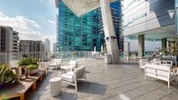 Located in the heart of Downtown Los Angeles, this rooftop amenity level at 705 W 9th St offers a compelling blend of modern design and outdoor living set against a dramatic urban backdrop. The centerpiece of the space is a resort-style swimming pool with crystal-clear water, flanked by a generous sun deck furnished with rows of chaise lounges and shaded seating areas beneath a partially covered pavilion supported by bold concrete columns. Floor-to-ceiling glass walls enclose interior lounge areas, allowing unobstructed views of the surrounding skyline from virtually every vantage point.

Adjacent to the pool deck, an elevated garden terrace provides a striking contrast, featuring lush, meticulously maintained landscaping with native shrubs, ornamental grasses, succulents, trees, and decorative stone pathways. Weathered wood boardwalks guide visitors through the greenery, creating a tranquil retreat above the city. An outdoor kitchen and grill station are conveniently integrated into the terrace, offering space for entertaining.

Throughout the amenity level, large-format stone tile paving, glass railings, and clean architectural lines contribute to a contemporary aesthetic. Abundant natural light, open-air exposure, and panoramic views of Downtown Los Angeles's iconic high-rise skyline define the overall ambiance, making this rooftop an exceptional urban outdoor destination.