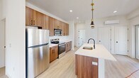 This modern 3-bedroom, 2-bathroom home in Dayton, NJ offers a thoughtfully designed single-floor layout filled with clean lines and contemporary finishes throughout. Light wood-tone flooring runs seamlessly across the entire unit, complementing the crisp white walls and creating a bright, cohesive aesthetic.

The kitchen is a standout feature, showcasing warm wood cabinetry with matte black hardware, white quartz countertops, stainless steel appliances, and a central island with a built-in sink and stylish pendant lighting. A white subway tile backsplash adds a classic touch to the modern design.

The living room is generously proportioned, bathed in natural light from multiple windows that offer views of the surrounding neighborhood. Each bedroom is well-sized, with the spacious primary bedroom featuring a wall-mounted mini-split system for individual climate control. The secondary bedrooms also receive abundant natural light through large windows.

Both bathrooms are elegantly appointed with floating wood vanities, white quartz countertops, matte black fixtures, large-format tile flooring, and framed mirrors. One bathroom includes a soaking tub with floor-to-ceiling marble-style tile surround. A hallway connects all rooms, completing this clean and functional floor plan.