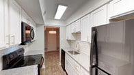 The Berkly's 1-bedroom, 1-bathroom floor plan is thoughtfully designed across a single level, combining updated finishes with a functional layout. The kitchen serves as a standout feature, showcasing white shaker-style cabinetry, granite-look countertops, a classic white subway tile backsplash, and wood-look flooring. Black stainless steel appliances, including a range, microwave, and refrigerator, complement the space, while a stainless steel sink with a modern faucet adds a polished touch. Recessed skylight-style fixtures provide bright, even overhead lighting.

The living and dining areas are carpeted and generously proportioned, with neutral gray walls and a pendant light fixture defining the dining space. A door with a window panel connects the living area to the outdoors, allowing natural light to filter in.

The bedroom is spacious and carpeted, featuring a textured ceiling, neutral tones, a window for natural light, and access to a dedicated closet. The bathroom is finished with large marble-patterned wall tiles surrounding the tub-shower combination, paired with a clean white toilet and granite-look countertops, creating a crisp, contemporary aesthetic throughout.