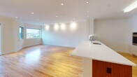 Located at 146–166 Marion St in Brookline, MA, this single-floor residence offers a well-designed layout that balances open living spaces with functional, private areas. The heart of the home is an expansive open-plan living and kitchen area, featuring warm hardwood flooring that flows seamlessly throughout. Recessed lighting illuminates the space, complemented by natural light streaming through windows that offer views of the surrounding Brookline neighborhood. Crown molding adds a refined architectural touch to the living areas.

The kitchen is thoughtfully appointed with rich wood cabinetry paired with crisp white upper cabinets and countertops, stainless steel appliances including a refrigerator, wall oven, cooktop, and dishwasher. A breakfast bar peninsula provides additional prep and seating space. A built-in pantry with open shelving offers generous storage near the entry.

The bedroom is a bright, comfortable retreat with hardwood floors, crown molding, and a large window framing neighborhood rooftop views. A dedicated room provides flexible use as an additional bedroom or office, also finished with hardwood floors and recessed lighting.

The bathroom is designed for accessibility, featuring light-toned porcelain tile flooring, a combination tub and shower with full tile surround, grab bars, and a clean white vanity with a neutral countertop — all finished in a calm, neutral palette.