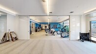 Located at 101 Bryce Lane in King of Prussia, PA, this single-floor fitness studio offers a generously sized, well-appointed workout facility designed to accommodate a wide range of exercise needs. The space is defined by a clean, modern aesthetic, with crisp white ceilings, bold blue accent walls, and light-toned flooring throughout that together create an energizing yet professional atmosphere.

The main workout floor is expansive, housing a comprehensive selection of cardio equipment including treadmills, ellipticals, stationary bikes, and rowing machines, all arranged to maximize space and flow. A dedicated strength training zone features multi-station cable machines, weight benches, a full dumbbell rack, and stability ball storage, catering to both functional and resistance training. Floor-to-ceiling mirrors line key areas of the studio, visually expanding the space and supporting proper form during exercise.

Linear recessed lighting runs along the ceiling, providing bright, even illumination throughout. Large glass doors and floor-to-ceiling windows along one wall invite abundant natural light and offer views of the outdoor surroundings, creating a refreshing connection to the exterior. Sliding partition walls allow for flexible configuration of the space, enabling separation of workout zones as needed. The studio also includes a small private room with glass-panel doors, suitable for focused training or consultations. Overall, the space delivers a polished, functional fitness environment.