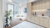 Located at 1114 Rue Saint-Antoine Ouest in the heart of Montréal, this efficiently designed two-bedroom, one-bathroom unit offers a thoughtful layout across a single floor. The open living and kitchen area serves as the centerpiece of the unit, showcasing floor-to-ceiling windows that flood the space with natural light and frame sweeping city views. The kitchen features sleek, light wood cabinetry that extends to the ceiling, a marble-effect backsplash, an undermount sink with a matte black faucet, and under-cabinet lighting — delivering a refined, contemporary aesthetic. Light hardwood flooring runs throughout, enhancing the bright, airy ambiance. The primary bedroom benefits from a large window with expansive urban views, while the second bedroom offers a clean, minimalist design with direct access to the main living area. The bathroom is well-appointed with marble-style tile flooring, a floating wood vanity with stone countertop, built-in open shelving, and a full tub-shower combination with white subway tile surround. A hallway with scalloped-edge door frames adds a subtle architectural detail. The unit also includes in-unit laundry. The overall design is modern and cohesive, emphasizing clean lines, neutral tones, and smart use of space.