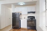 Located at 1440 R St NW in Washington, DC's vibrant Logan Circle neighborhood, this one-bedroom, one-bathroom unit offers a efficiently designed single-floor layout. The open-concept living and dining area flows directly into the kitchen, creating a cohesive and functional common space. The kitchen is equipped with black appliances — including a full-size refrigerator and gas range — paired with crisp white cabinetry and a single-basin sink, all set atop hardwood-style flooring. Natural light filters into the combined living and dining space through a window fitted with horizontal blinds, adding brightness to the neutral-toned walls. The carpeted bedroom is notably well-lit, featuring multiple windows that allow generous natural light to fill the room, lending an airy feel despite the cozy footprint. A dedicated closet provides storage within the bedroom. The unit also includes a full bathroom, a utility room, and a hallway that connects the various spaces. The layout, as seen in the dollhouse view, is thoughtfully arranged to maximize every square foot, making this an ideal city residence for those seeking a manageable, low-maintenance space in a prime Washington, DC location.