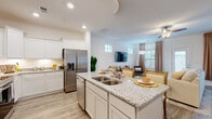 This two-story home offers a thoughtfully designed layout that balances style and functionality across both levels. The main floor greets you with a welcoming entryway featuring light wood-look flooring, white wainscoting accents, and a carpeted staircase with warm wood railings leading to the upper level. The open-concept living area flows seamlessly into the dining space and kitchen, creating an ideal environment for everyday living and entertaining. The kitchen is a standout, boasting white shaker-style cabinetry with crown molding, granite countertops, stainless steel appliances including a French door refrigerator and range, a large center island with a double sink, and under-cabinet lighting. The bright living room features a ceiling fan, recessed lighting, and high transom windows that invite natural light. A dedicated dining area is accented by tasteful artwork and shares the same light-filled ambiance. Upstairs, the primary bedroom impresses with a tray ceiling, ceiling fan, plush carpeting, and generous natural light from multiple windows. A spacious walk-in closet with wire shelving provides ample storage. The home also includes a dedicated laundry room with side-by-side washer and dryer and overhead shelving, completing this well-appointed residence.
