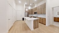 Located at 8350 Highway 290 W in Austin, TX, this well-appointed 2-bedroom, 2-bathroom residence offers a thoughtfully designed layout with modern finishes throughout. Light wood-style flooring flows consistently across the living areas and bedrooms, creating a bright and cohesive aesthetic.

The kitchen is a standout feature, showcasing flat-panel wood-tone cabinetry extending to the ceiling, a textured tile backsplash, and a large quartz-topped island with an undermount sink and pendant lighting above. Stainless steel appliances, including a French door refrigerator, range, and over-the-range microwave, complete the contemporary look.

The primary bedroom is generously sized and includes a dedicated walk-in closet with rod storage. Its en-suite bathroom features a single-sink vanity with wood cabinetry, quartz countertop, a glass-enclosed walk-in shower with tile surround, and stone-look tile flooring. The second bathroom offers a tub-shower combination, a wood-toned vanity, and matching finishes. The second bedroom is bright and well-proportioned, also served by its own walk-in closet.

A private balcony with metal railing provides outdoor space with views of the surrounding community. Recessed lighting throughout adds to the clean, modern ambiance of this Austin residence.