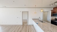 Located at 11613 Vista Terrace Way in Knoxville, Tennessee, this single-floor residence offers a thoughtfully designed open-concept layout with a clean, contemporary aesthetic throughout. The kitchen serves as a central highlight, anchored by a large island with a granite countertop and double stainless steel sink, illuminated by stylish pendant lighting. Rich, warm-toned cabinetry provides generous storage and pairs well with stainless steel appliances, including a refrigerator, range, and microwave. Light wood-style flooring flows through the main living areas, complementing the bright white walls and creating an airy, cohesive feel. The living area is generously proportioned, featuring a ceiling fan and large windows that invite abundant natural light and views of the surrounding Knoxville landscape. The bedrooms are well-sized, with plush carpeting in select rooms and ample natural light from multiple windows. The bathroom showcases a granite-topped vanity with dual sinks, rich cabinetry, and backlit mirrors, adding a refined touch. Additional utility space includes a dedicated laundry area with wire shelving and hookups. The overall ambiance is fresh, modern, and move-in ready, offering comfortable and stylish single-floor living.
