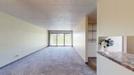 Located at 2101 Oakwood Rd in Ames, Iowa, this four-bedroom, one-bathroom unit offers a functional and practical layout across a single floor. The open living area is finished with neutral-toned carpet and warm beige walls, creating a clean and understated aesthetic. A ceiling fan with a light fixture anchors the living space, which also features a sliding glass door that fills the room with natural light and provides views of the surrounding greenery outside. The galley-style kitchen is well-appointed with light maple cabinetry, granite-look countertops, tile flooring, a skylight panel ceiling, and a full suite of black and stainless appliances including a refrigerator, electric range, and dishwasher. The four bedrooms are carpeted and offer ample wall space, with several rooms benefiting from windows with blinds and built-in closet areas complete with hanging rods and shelving. The primary bedroom includes a ceiling fan and direct access to a closet nook with a window. The shared full bathroom features tile flooring, a tub-shower combination, a white vanity, and a textured ceiling. Throughout the unit, a consistent neutral color palette and practical finishes provide a comfortable and move-in-ready living environment.