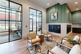 Located at 397 N Central Ave in Hapeville, Georgia, this single-floor community space offers a well-appointed and thoughtfully designed environment spanning a generous footprint. The layout includes a welcoming hallway and an open living room area that together create a seamless flow throughout the space.

The interior design blends contemporary and organic elements, anchored by wide-plank light oak hardwood flooring that runs throughout. Sage green shiplap accent walls rise to meet crisp white upper walls, creating a distinctive two-tone aesthetic that lends warmth and character. Exposed wood beam detailing on the ceiling adds an architectural dimension, while pendant lighting and recessed fixtures provide layered illumination.

The lounge area features a curated seating arrangement with neutral-toned armchairs and patterned area rugs, centered around a cluster of built-in mailboxes, making it a functional yet inviting hub. Floor-to-ceiling steel-framed glass partitions define a private conference or coworking room furnished with a long communal wood table and industrial-style seating — ideal for collaborative use.

Large black-framed windows flood portions of the space with abundant natural light and offer views to the exterior surroundings. A statement chandelier with a geometric metal frame and lush greenery serves as a dramatic focal point in the lounge. The overall ambiance is modern, cohesive, and refined, balancing comfort with purposeful design.