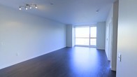 This contemporary single-floor space offers a clean, minimalist aesthetic defined by a thoughtful combination of materials and natural light. The main living area is anchored by rich, dark hardwood flooring that contrasts elegantly with the crisp white walls and smooth white ceiling, creating a sleek and polished atmosphere throughout.

A standout feature of the space is the expansive floor-to-ceiling window along one wall, which draws in abundant natural light and provides open views of the surrounding exterior. This large glazed opening gives the room an airy, open feel and serves as a natural focal point.

Overhead, a track lighting fixture is mounted to the ceiling, offering flexible and functional illumination to complement the natural light. The ceiling is smooth and unadorned, contributing to the space's modern, uncluttered character.

The layout is open and versatile, with generous proportions that allow for a variety of furniture arrangements and uses. Clean baseboards and well-finished corners reflect careful attention to detail in the construction. Overall, this space combines modern finishes, natural light, and an open floor plan to create a bright, inviting, and highly functional environment.