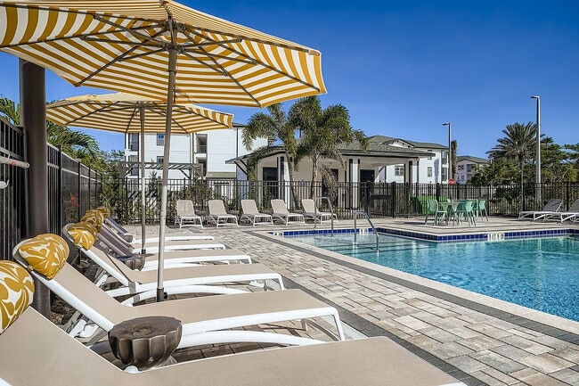 Premium outdoor pool area with elegant sun loungers, striped umbrellas, and lush greenery, perfect for relaxation and leisure. - Magnolia at Palm Bay