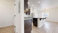 This two-story, three-bedroom, two-bathroom home offers a thoughtfully designed layout across two floors. The main level welcomes residents through a dedicated entrance that leads into a bright living room featuring plush carpeting and soaring ceilings with staircase access. Adjacent to the living area, the dining room is accented by a stylish chandelier and a large window that fills the space with natural light, while light wood-look flooring flows seamlessly underfoot. The kitchen is a standout feature, showcasing rich dark espresso cabinetry, granite countertops, stainless steel appliances including a gas range, microwave, and refrigerator, and a functional breakfast bar island ideal for casual dining. The upper floor houses all three bedrooms, each finished with soft neutral carpeting and windows for natural light. The spacious primary bedroom offers generous proportions, while the secondary bedrooms each include sliding closet doors for practical storage. Both bathrooms are appointed with dark wood vanities and wood-look tile flooring, maintaining a consistent design aesthetic throughout. A hallway and dedicated closet on the upper level add to the home's organizational convenience. Clean white walls, recessed lighting, and consistent finishes throughout create a cohesive, move-in-ready interior.