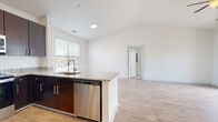 Located at 3201 Windshire Ln in Charlotte, NC, this two-story home offers three bedrooms and two bathrooms across a well-designed layout. The main living level is generously proportioned, featuring an open-concept kitchen and living area bathed in natural light from large windows. The kitchen is outfitted with rich dark cabinetry, granite countertops, a peninsula with sink, and a full suite of stainless steel appliances including a refrigerator, range, microwave, and dishwasher. Light wood-tone flooring runs throughout the main living areas, adding warmth and continuity. The living room is highlighted by vaulted ceilings, a ceiling fan, and sliding glass doors that open to a balcony with outdoor views. The bedrooms are carpeted and bright, each offering closet space with built-in shelving. The primary bedroom is a comfortable size with its own dedicated closet. The bathrooms are clean and functional, featuring dark vanity cabinetry with light countertops and a tiled shower-tub combination. The attached garage on the lower level provides convenient parking and additional storage. Throughout the home, crisp white walls and an abundance of natural light create a fresh, airy atmosphere.
