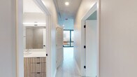 Located in Chicago's Uptown neighborhood at 4600–4668 N Winthrop Ave, this contemporary single-floor unit showcases a clean, modern aesthetic throughout. The open-concept layout connects the living area and kitchen seamlessly, with large floor-to-ceiling windows flooding the space with natural light and framing sweeping city views of the surrounding Chicago skyline and rooftops. Light-tone luxury vinyl plank flooring runs throughout the main living areas, complementing the exposed concrete ceilings that lend the space an industrial-modern character. The well-appointed kitchen features textured wood-grain cabinetry, a white subway tile backsplash, a stainless steel appliance suite including a refrigerator, gas range, microwave, and dishwasher, and a sleek undermount sink. The bedroom continues the floor-to-ceiling window design, offering generous natural light and urban views. A hallway connects the living spaces to the bathroom, which is finished with large-format tile flooring, wood-grain vanity cabinetry, a white countertop, and matte black hardware accents that echo throughout the unit. Louvered closet doors add a refined touch to the corridor, while recessed lighting ensures a well-lit, welcoming ambiance throughout this thoughtfully designed urban residence.