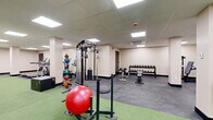 Located at 90 N Swan St in Albany, New York, this single-floor exercise facility offers a comprehensive fitness environment designed to accommodate a wide range of workout needs. The space is divided into distinct functional zones, all unified by a clean, neutral color palette of warm beige walls and dark baseboards. Recessed panel lighting set into a drop-tile ceiling provides consistent, even illumination throughout.

The main workout area features a dedicated green turf section ideal for functional training and agility drills, complemented by an array of equipment including a cable crossover machine, medicine balls, stability balls, plyo boxes, and a sled. Adjacent to the turf, a cardio zone houses multiple treadmills and elliptical machines, each equipped with individual digital screens for interactive workout tracking.

A free weights area offers a full rack of dumbbells alongside adjustable benches, catering to strength training routines. Additional strength equipment, including a multi-station cable machine and a squat rack with weight plates, is strategically positioned throughout the space. Durable rubber flooring covers the non-turf areas, providing both safety and functionality.

A separate, open-plan room with polished rubber flooring and ceiling-mounted HVAC offers a versatile, equipment-free space suitable for stretching, yoga, or group classes. Multiple entry points via black-framed doors ensure smooth flow throughout the facility.