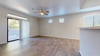 This single-floor unit is designed with a clean, contemporary aesthetic and a neutral color palette throughout. The main living area features wood-look hard-surface flooring and a ceiling fan with integrated lighting. Two high-set windows allow natural light while maintaining privacy, and a sliding glass door with vertical blinds provides direct access to an outdoor space.

A second room with matching hard-surface flooring also opens to an outdoor area through a sliding glass door topped by a transom window, offering additional natural light and exterior views.

The kitchen is efficiently laid out in a U-shaped configuration and equipped with stainless steel appliances, including a refrigerator, range, microwave, and dishwasher. White upper cabinetry contrasts with gray lower cabinets, complemented by light countertops and wood-look tile flooring.

The bedrooms are carpeted and well-lit by large windows fitted with horizontal blinds. Each room offers a comfortable sense of space with clean wall surfaces.

Two bathrooms mirror each other in design, featuring gray cabinetry, white countertops, large vanity mirrors, and wood-look tile flooring. One bathroom includes a shower-tub combination, providing full functionality throughout the unit.