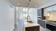 This contemporary two-floor residence is defined by clean lines, an open layout, and high-end finishes that create a bright, sophisticated living environment. The main level showcases a dramatic double-height living area flooded with natural light through two tiers of windows, with light wood-tone flooring running throughout. The gourmet kitchen is a standout feature, equipped with premium stainless steel appliances including a gas range, built-in oven, and French door refrigerator. Contrasting dark lower cabinetry pairs with crisp white upper cabinets, while a generous island with a quartz countertop and undermount sink serves as both a prep station and gathering space. Elegant pendant lighting completes the kitchen's polished aesthetic. The bathrooms are finished with large-format tile flooring, dark vanities with white countertops, and glass-enclosed showers, maintaining the home's modern sensibility. The lower floor features carpeted bedrooms with mirrored sliding-door closets offering ample built-in storage. A staircase connects the two levels, with additional hallway space and recessed lighting providing a seamless transition between floors. Throughout the residence, white walls, recessed lighting, and consistent material choices create a cohesive and refined atmosphere.