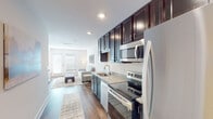 This single-floor residence offers a thoughtfully designed layout that balances functionality and modern style throughout. The galley-style kitchen is a standout feature, showcasing rich dark espresso cabinetry extending to the ceiling for generous storage, light granite countertops, and a full suite of stainless steel appliances including a French-door refrigerator, electric range, built-in microwave, and dishwasher. Recessed lighting illuminates the space, which flows seamlessly into the open living area. The living room is bright and welcoming, with warm hardwood-style flooring, a neutral color palette, and a glass-paneled entry door that invites natural light. Two bedrooms provide comfortable retreats, each featuring plush carpeting, soft neutral walls, and windows that bring in outside light and views. The bathroom is finished with classic black-and-white mosaic tile flooring, a dark vanity with a white countertop, and a large mirror. A dedicated laundry area houses a stacked washer and dryer unit alongside built-in shelving, adding practical convenience. Throughout the residence, clean lines, consistent finishes, and recessed lighting create a cohesive, move-in-ready living environment.