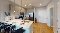 Located at Hopson Road in Durham, NC, this single-floor residence showcases a thoughtfully designed, modern interior with a cohesive contemporary aesthetic. The open-concept kitchen serves as a central highlight, featuring light wood-toned cabinetry, white subway tile backsplash, quartz countertops, and a peninsula with an undermount stainless steel sink illuminated by pendant lighting. Stainless steel appliances, including a French door refrigerator, electric range, microwave, and dishwasher, complete the well-appointed cooking space. Wood-look flooring flows throughout the main living areas, adding warmth to the light gray color palette.

The bedrooms are comfortably scaled, each offering large windows that invite natural light and are dressed with neutral-toned drapes. The primary bedroom connects to a well-organized walk-in closet with wire shelving systems and direct access to a private bathroom featuring a wood-toned vanity, framed mirror, and a glass-enclosed shower with white subway tile surround. A second bathroom provides additional convenience for residents or guests. The overall layout, as seen in the floor plan view, is efficiently arranged to maximize livability across the single level.