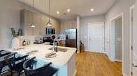 Located at Hopson Road in Durham, NC, this single-floor residence showcases a thoughtfully designed, modern interior with a cohesive contemporary aesthetic. The open-concept kitchen serves as a central highlight, featuring light wood-toned cabinetry, white subway tile backsplash, quartz countertops, and a peninsula with an undermount stainless steel sink illuminated by pendant lighting. Stainless steel appliances, including a French door refrigerator, electric range, microwave, and dishwasher, complete the well-appointed cooking space. Wood-look flooring flows throughout the main living areas, adding warmth to the light gray color palette.

The bedrooms are comfortably scaled, each offering large windows that invite natural light and are dressed with neutral-toned drapes. The primary bedroom connects to a well-organized walk-in closet with wire shelving systems and direct access to a private bathroom featuring a wood-toned vanity, framed mirror, and a glass-enclosed shower with white subway tile surround. A second bathroom provides additional convenience for residents or guests. The overall layout, as seen in the floor plan view, is efficiently arranged to maximize livability across the single level.