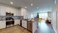 Located at 1000 Schindler Dr in South Amboy, NJ, this modern single-floor residence offers a thoughtfully designed open-concept layout with contemporary finishes throughout. The kitchen is a standout feature, showcasing white shaker cabinetry, gray quartz countertops, a herringbone tile backsplash, and a full suite of stainless steel appliances including a gas range, microwave, dishwasher, refrigerator, and a built-in wine cooler. A central island with bar seating seamlessly connects the kitchen to the dining and living areas, creating an ideal space for entertaining. The living room is bathed in natural light from large windows offering open outdoor views, and features durable light wood-style flooring that flows throughout the space. The primary bedroom is generously proportioned with a large window, ample natural light, and a private en-suite bathroom complete with a walk-in glass shower, white vanity cabinetry, and tile flooring. A second bedroom offers similar comfort and brightness. The secondary bathroom features a full tub-shower combination, white vanity, and tile flooring. Recessed lighting, neutral tones, and clean architectural lines contribute to the home's bright, modern ambiance.