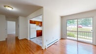 This 1-bedroom, 1-bathroom residence offers a practical and comfortable single-floor layout. Warm hardwood flooring flows consistently throughout the living areas and bedroom, lending a cohesive and inviting character to the space. The living room is bright and open, benefiting from a sliding glass door that opens to a private balcony overlooking a green outdoor area, allowing natural light to fill the room. Baseboard heating is present throughout, ensuring consistent warmth across all rooms. The kitchen is a functional U-shaped space featuring rich, warm-toned wood cabinetry, white appliances including a refrigerator, range, and dishwasher, and light tile flooring. A window above the sink provides additional natural light. The bedroom is a comfortable size, featuring two closets with sliding doors, offering ample storage, along with a window that frames a pleasant outdoor view. The bathroom is finished with white subway tile wainscoting, a wood-framed vanity with a marble-style countertop, and a rectangular mirror. The overall layout is efficient and well-organized, making practical use of the available space throughout.