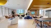This amenities lounge in Miami, FL offers a generously proportioned single-floor layout thoughtfully designed for both relaxation and productivity. The main living area is a standout centerpiece, bathed in natural light streaming through floor-to-ceiling windows that frame lush greenery and urban skyline views. Curated furnishings — including plush leather seating, deep green velvet chairs, and bold blue patterned rugs — lend a vibrant, sophisticated character to the space. A built-in entertainment wall with backlit shelving and a warm wood-paneled ceiling creates an intimate lounge nook, while a striking sculptural pendant light anchors the broader social gathering area. The open layout transitions seamlessly between distinct seating vignettes, punctuated by potted fiddle-leaf fig trees and artful décor. A dedicated office area features glass-walled workspaces enclosed by sleek sliding doors, offering privacy while maintaining visual connectivity to the lounge. Clean-lined desks, ergonomic seating, and curated artwork — including a large-format musical instrument print — give the workspace a refined, creative atmosphere. Polished tile flooring and a crisp white palette run throughout, tying together the varied zones with a cohesive, modern aesthetic. A colorful arched doorway adds a playful design accent along the corridor connecting the space's key areas.
