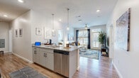 This thoughtfully designed single-floor residence offers four bedrooms and four bathrooms, making it an ideal layout for shared or family living. The open-concept kitchen and living area serves as the heart of the home, featuring light wood-tone flooring, recessed lighting, and abundant natural light streaming through large windows and a glass door that opens to an outdoor area. The kitchen is equipped with stainless steel appliances, white upper cabinetry, a granite-topped island with bar seating for four, and stylish pendant lighting overhead. The adjoining living area is bright and welcoming, complete with a ceiling fan and a direct view to the outdoors.

Each of the four bedrooms is carpeted for comfort and includes its own dedicated bathroom and walk-in closet outfitted with wire shelving systems, providing generous storage for each resident. The bedrooms feature ceiling fans, windows for natural light, and enough space to accommodate a bed and a dedicated workspace. The bathrooms are consistently finished with granite-topped vanities, grey cabinetry with black hardware, and wood-look flooring, while select bathrooms include a tub-shower combination. A connecting hallway ties the private quarters together, creating a functional and cohesive floor plan throughout the residence.
