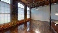This single-floor space masterfully combines industrial heritage with contemporary design, creating a striking and functional environment throughout. The most commanding architectural feature is the exposed original brick wall, punctuated by tall arched windows that flood the interior with natural light. Overhead, warm wood-beam ceilings and visible ductwork reinforce the industrial aesthetic, while a large ceiling fan ensures comfortable airflow across the expansive open area.

Polished concrete floors run consistently throughout, lending a sleek, cohesive look that complements the raw structural elements. Original heavy timber columns add character and structural authenticity to the space.

The kitchen is well-appointed with white shaker-style cabinetry, dark granite countertops, a mosaic tile backsplash, stainless steel appliances including a refrigerator, range, and microwave, as well as a central island with pendant lighting suspended from the beamed ceiling. An adjacent walk-in pantry provides generous storage.

The bathroom features matching white cabinetry with dark countertops, polished concrete floors, and clean, neutral finishes. A dedicated walk-in closet with wire shelving offers practical storage. Track lighting throughout the space provides flexible, adjustable illumination, completing the modern-industrial character of this unique property.