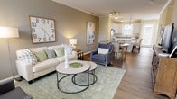 The Willow floor plan in Canton, Michigan, is a thoughtfully designed two-story home offering two bedrooms and two and a half bathrooms. The main level features an open-concept layout where the living room, dining area, and kitchen flow seamlessly together, finished with durable wood-look flooring and crown molding throughout. The living room receives natural light through multiple windows dressed with patterned drapes, creating a bright and welcoming atmosphere. The kitchen is well-appointed with white shaker-style cabinetry, granite countertops, a white subway tile backsplash, stainless steel appliances, and a center island, making it both functional and visually appealing. A half bathroom on the main level provides added convenience for guests. A staircase leads to the upper floor, where both bedrooms are located. The primary bedroom is carpeted and features crown molding, ample natural light, and access to a walk-in closet. The full bathroom on this level includes white cabinetry with granite countertops and a glass-enclosed shower. A dedicated laundry closet with a full-size washer and dryer adds practicality to the upper level. Overall, the Willow offers a clean, modern aesthetic with functional, well-organized living spaces.