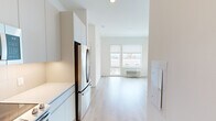 Located at 244 St Pauls Ave in Jersey City, NJ, this modern two-bedroom residence offers a thoughtfully designed single-floor layout with a clean, contemporary aesthetic throughout. Light-toned hardwood flooring runs seamlessly across the entire space, complementing the crisp white walls and creating a bright, cohesive feel.

The kitchen is well-appointed with sleek white cabinetry extending floor to ceiling, stainless steel appliances including a French door refrigerator, built-in microwave, electric range, and a dishwasher. Ample counter space and open shelving add both function and style to this galley-style kitchen.

The open living area flows naturally from the kitchen and is bathed in natural light through large windows that frame views of the surrounding Jersey City neighborhood. The spacious primary bedroom features a dual-window configuration offering expansive city views, while both bedrooms are finished with the same warm hardwood flooring and neutral white walls, providing a clean and versatile canvas.

A louvered closet door adds a practical storage element near the kitchen entrance, and the unit features a keypad-secured front entry door. The overall design is minimalist and modern, making this a well-suited residence for those seeking a functional, light-filled home in Jersey City.