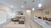 This well-designed single-floor residence offers a cohesive and modern living experience through its open-concept layout and consistent neutral palette. Light wood-style flooring flows seamlessly throughout, unifying the spaces and enhancing the bright, airy ambiance created by recessed lighting and large windows dressed with clean white blinds.

The kitchen serves as a central hub of the home, featuring dark espresso cabinetry, granite countertops, a peninsula with pendant lighting, and a full suite of stainless steel appliances including a refrigerator, range, microwave, and dishwasher. This area transitions naturally into the dining space and the generous living room, which benefits from abundant natural light through multiple windows and a sliding glass door.

The living area provides a comfortable and versatile space, while a secondary sitting nook near the entry offers additional flexibility. The bedroom is a calm retreat, highlighted by a large window that invites natural light and a ceiling fan for added comfort.

The bathroom impresses with its spacious layout, featuring a granite-topped dual vanity with dark cabinetry, a large mirror, a tiled walk-in shower, and light wood-style flooring that carries the home's design language throughout. Clean lines and neutral tones make this a polished and functional space overall.
