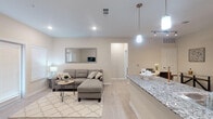 This well-designed single-floor residence offers a cohesive and modern living experience through its open-concept layout and consistent neutral palette. Light wood-style flooring flows seamlessly throughout, unifying the spaces and enhancing the bright, airy ambiance created by recessed lighting and large windows dressed with clean white blinds.

The kitchen serves as a central hub of the home, featuring dark espresso cabinetry, granite countertops, a peninsula with pendant lighting, and a full suite of stainless steel appliances including a refrigerator, range, microwave, and dishwasher. This area transitions naturally into the dining space and the generous living room, which benefits from abundant natural light through multiple windows and a sliding glass door.

The living area provides a comfortable and versatile space, while a secondary sitting nook near the entry offers additional flexibility. The bedroom is a calm retreat, highlighted by a large window that invites natural light and a ceiling fan for added comfort.

The bathroom impresses with its spacious layout, featuring a granite-topped dual vanity with dark cabinetry, a large mirror, a tiled walk-in shower, and light wood-style flooring that carries the home's design language throughout. Clean lines and neutral tones make this a polished and functional space overall.