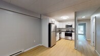This single-floor unit offers a practical and well-appointed layout designed for comfortable everyday living. Light wood laminate flooring runs consistently throughout the space, creating a cohesive and easy-to-maintain aesthetic. Neutral gray walls provide a versatile backdrop across all rooms.

The kitchen is equipped with a full suite of stainless steel appliances, including a refrigerator, electric range, and over-the-range microwave. White shaker-style cabinetry lines the walls, offering generous storage, while dark countertops provide contrast. The kitchen connects openly to the living area, which features baseboard heating and a smooth flow into adjacent spaces.

Two bedrooms provide comfortable living quarters, each featuring windows that allow natural light and views of the surrounding greenery. One bedroom includes access to a dedicated in-unit laundry closet with a stacked washer and dryer, as well as a spacious walk-in closet nearby.

Two bathrooms serve the unit — one featuring a full soaking tub with an integrated surround and built-in shelving, and the other a compact stand-up shower stall. Both bathrooms are finished with clean white fixtures and wood-tone flooring, maintaining the unit's consistent and functional design throughout.