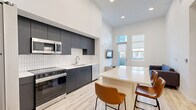 Located at 2555 Research Park Dr in Davis, CA, this contemporary 2-bedroom, 3-bathroom residence offers a well-designed single-floor layout. The open-concept kitchen and living area serves as the heart of the home, featuring dramatically high ceilings that amplify the sense of space. The sleek, modern kitchen is outfitted with dark matte cabinetry extending to the ceiling, a white subway tile backsplash, stainless steel appliances including a refrigerator, range, microwave, and dishwasher, and a white waterfall-edge island with bar seating. Light wood-tone flooring flows throughout, complementing the bright, neutral palette. The living area is bathed in natural light through tall windows with exterior views, and a glass-panel door leads to a private patio. Both bedrooms are comfortably scaled, with the generously sized primary bedroom offering ample closet space. The bathrooms are clean and modern, featuring tub-shower combinations and dark cabinetry vanities. Additional highlights include a dedicated laundry area, multiple closets for abundant storage, and a hallway connecting all rooms efficiently. The overall ambiance is clean, minimalist, and contemporary.