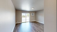 This single-story residence in Livermore, California offers a practical and well-organized layout comprising a living room, two bedrooms, a kitchen, and a connecting hallway. Throughout the main living areas, wood-look laminate flooring in a warm, medium-toned finish provides a cohesive and easy-to-maintain surface. The living room is a bright, open space featuring a sliding glass door that allows natural light to flood in while providing direct access to an outdoor area with views of surrounding greenery. A wall-mounted air conditioning unit serves the space for climate control.

The kitchen is efficiently designed in a U-shaped configuration, featuring honey-toned wood cabinetry, dark countertops, a double sink, and white appliances including a refrigerator, dishwasher, and range. A ceiling fan with a light fixture adds air circulation to this area.

Both bedrooms are carpeted in a neutral beige tone, each equipped with sliding-door closets featuring arched panel doors. Windows fitted with vertical blinds allow natural light while maintaining privacy. The neutral taupe wall palette carries consistently throughout the unit, lending a calm and uniform ambiance to the overall space.