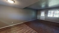 This two-floor home offers a functional and straightforward layout finished in a consistent neutral gray palette throughout. The main living area greets visitors through a white-paneled entry door and features a combination of wood-look hard flooring and dark brown carpet, providing a clear delineation between spaces. Textured ceilings add character to the main level, while ceiling fans are present in multiple rooms for added comfort. The kitchen is equipped with white cabinetry, a double stainless steel sink, and light countertops, with a window above the sink that allows natural light to filter in. A compact half bathroom on the main level includes wood-look flooring, a pedestal-style vanity, and a window with blinds. Upstairs, several generously sized bedrooms feature plush dark carpet, ceiling fans, and windows that bring in natural light. A full bathroom serves the upper level, offering a wide vanity with a single-basin sink, gray countertops, white tile accents, and a mirrored medicine cabinet with overhead lighting. Additional spaces include a lower-level room with paneled walls and a louvered closet door, suitable for flexible use. Throughout the home, white trim and baseboards provide clean visual contrast against the gray walls.