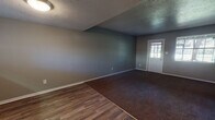 This two-floor home offers a functional and straightforward layout finished in a consistent neutral gray palette throughout. The main living area greets visitors through a white-paneled entry door and features a combination of wood-look hard flooring and dark brown carpet, providing a clear delineation between spaces. Textured ceilings add character to the main level, while ceiling fans are present in multiple rooms for added comfort. The kitchen is equipped with white cabinetry, a double stainless steel sink, and light countertops, with a window above the sink that allows natural light to filter in. A compact half bathroom on the main level includes wood-look flooring, a pedestal-style vanity, and a window with blinds. Upstairs, several generously sized bedrooms feature plush dark carpet, ceiling fans, and windows that bring in natural light. A full bathroom serves the upper level, offering a wide vanity with a single-basin sink, gray countertops, white tile accents, and a mirrored medicine cabinet with overhead lighting. Additional spaces include a lower-level room with paneled walls and a louvered closet door, suitable for flexible use. Throughout the home, white trim and baseboards provide clean visual contrast against the gray walls.